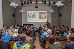 Ein voll besetzter Vortragssaal bei der Nacht der Wissenschaft in Düsseldorf; auf der Bühne wird ein Vortrag über Fotografie und künstliche Intelligenz gehalten.
